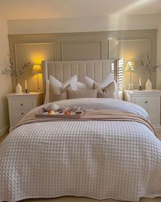 a bed with white sheets and pillows in a bedroom next to two lamps on either side of the bed