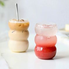 two small vases sitting next to each other on a white counter top, one with a straw sticking out of it