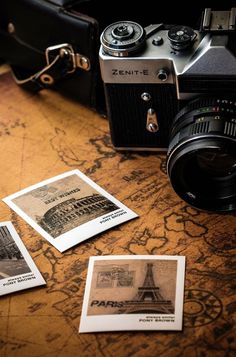 an old camera sitting on top of a wooden table next to some pictures and papers