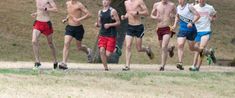 a group of young men running on a dirt road in front of a large tree