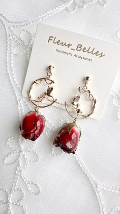 a pair of red earrings sitting on top of a piece of white fabric next to a card