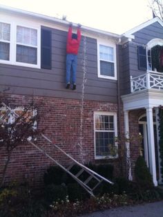 a man hanging from the side of a house with ladders in front of him