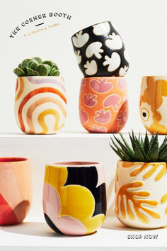 four different colored vases sitting on top of a white shelf next to a plant