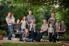 a group of people sitting on top of chairs in front of trees and bushes, posing for a family photo