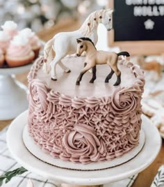 there is a pink cake with two horses on top and cupcakes in the background