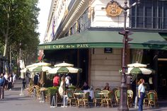 people sitting at tables in front of a cafe on a city street with green awnings