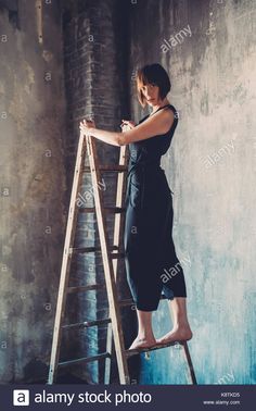 a woman standing on a ladder leaning against a wall - stock image