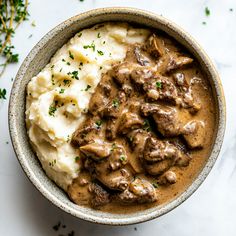 a bowl filled with mashed potatoes and meat covered in gravy on top of a white table