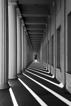 an empty hallway lined with columns and sun shining through the windows in black and white