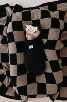 a black and white checkered blanket with a baby wearing a bow laying on it