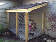 a woman and child are sitting in a dog ken with a fence around them outside