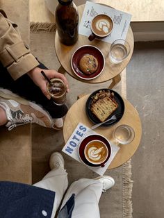 two people are sitting at a table with coffee and pastries on it, one is holding a drink