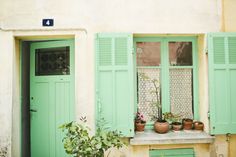 green shutters on the side of a building with potted plants