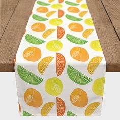 a white table runner with oranges and limes on it, sitting on a wooden surface