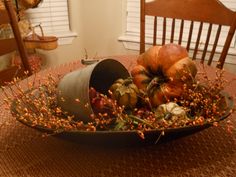 a bowl filled with pumpkins and gourds on top of a table next to a wooden chair