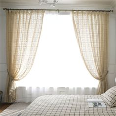 a bed sitting under a window next to a white wall with curtains on top of it