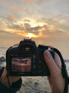 a person holding up a camera to take a photo with the sun setting in the background