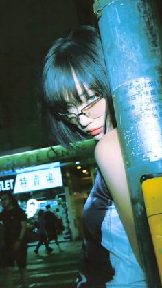 a woman with glasses leaning against a pole