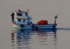 a man standing on top of a boat in the ocean next to another person holding a fishing pole