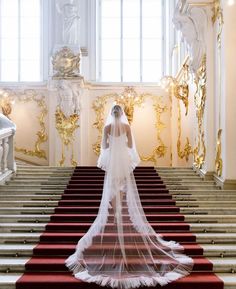 the bride is walking down the red carpeted stairs in her wedding dress and veil