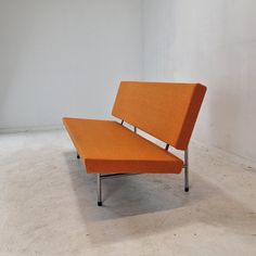 an orange couch sitting on top of a cement floor next to a white wall in a room