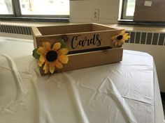 a wooden crate sitting on top of a table covered in white sheets and sunflowers