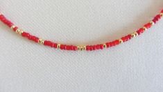 a red beaded necklace with gold beads on a white cloth covered surface, in the shape of a rectangle