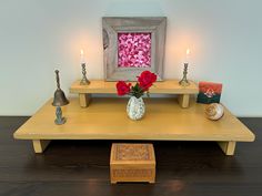 a wooden table topped with two vases filled with flowers and candles next to a painting