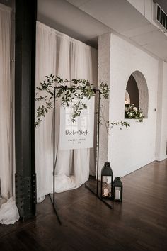 an empty room with white drapes and plants on the wall next to two black lanterns