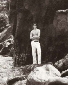 a man standing on top of a rock next to a river with his arms crossed