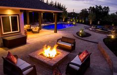 a fire pit sitting in the middle of a patio next to a swimming pool at night