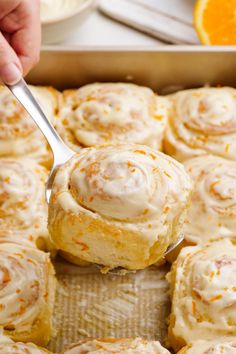 a person holding a spoon full of cinnamon rolls with icing on them and oranges in the background