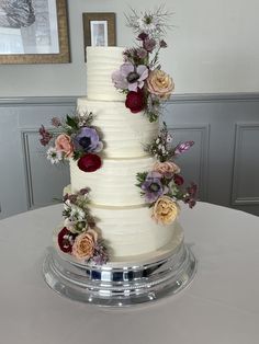 a three tiered white cake with flowers on the top and bottom is sitting on a round table