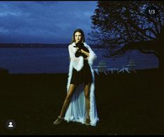 a woman standing in the grass with her hands on her hips wearing a fur coat