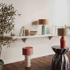 three vases and two lamps are on the shelf in front of each other, along with an olive tree