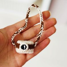 a hand holding a small crocheted object with an eye on it's end