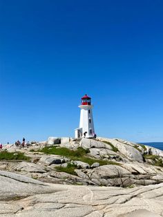 a lighthouse on top of a rocky outcropping near the ocean with people standing around it