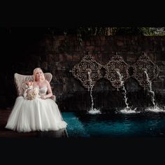 a woman in a wedding dress sitting on a chair next to a fountain with water pouring from it