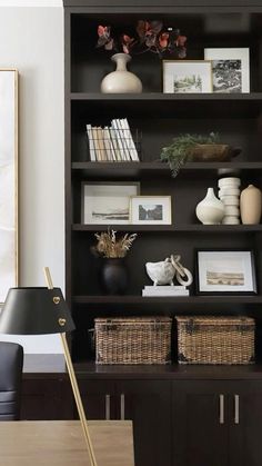 a black bookcase with baskets and pictures on it next to a lamp in a living room