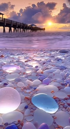 there are many glass pebbles on the beach by the water and pier at sunset or sunrise