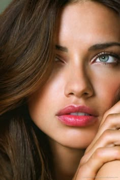 a woman with long brown hair and blue eyes is posing for the camera, her hand on her face