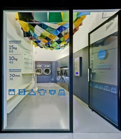 an empty laundry room with washers and dryer machines in the background, as seen through large glass doors