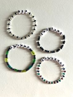 three bracelets with words written on them and beaded in white, green, black and red beads