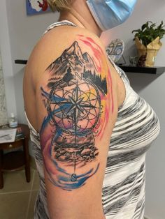 a woman with a mask on her face has a mountain and compass tattoo on her shoulder