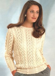 a woman wearing a white sweater and gray pants with her hands in her pockets, posing for the camera