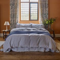 a bed sitting under a window next to a lamp and a table with a vase on it