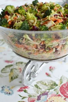 a glass bowl filled with broccoli and cranberries on top of a table