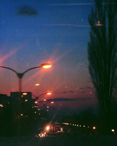 the sun is setting over an urban area with street lights and buildings in the background