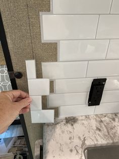 a hand is opening the door to a kitchen with white tile and black hardware on it