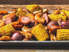 corn on the cob with sausage and potatoes in a metal dish sitting on a wooden table